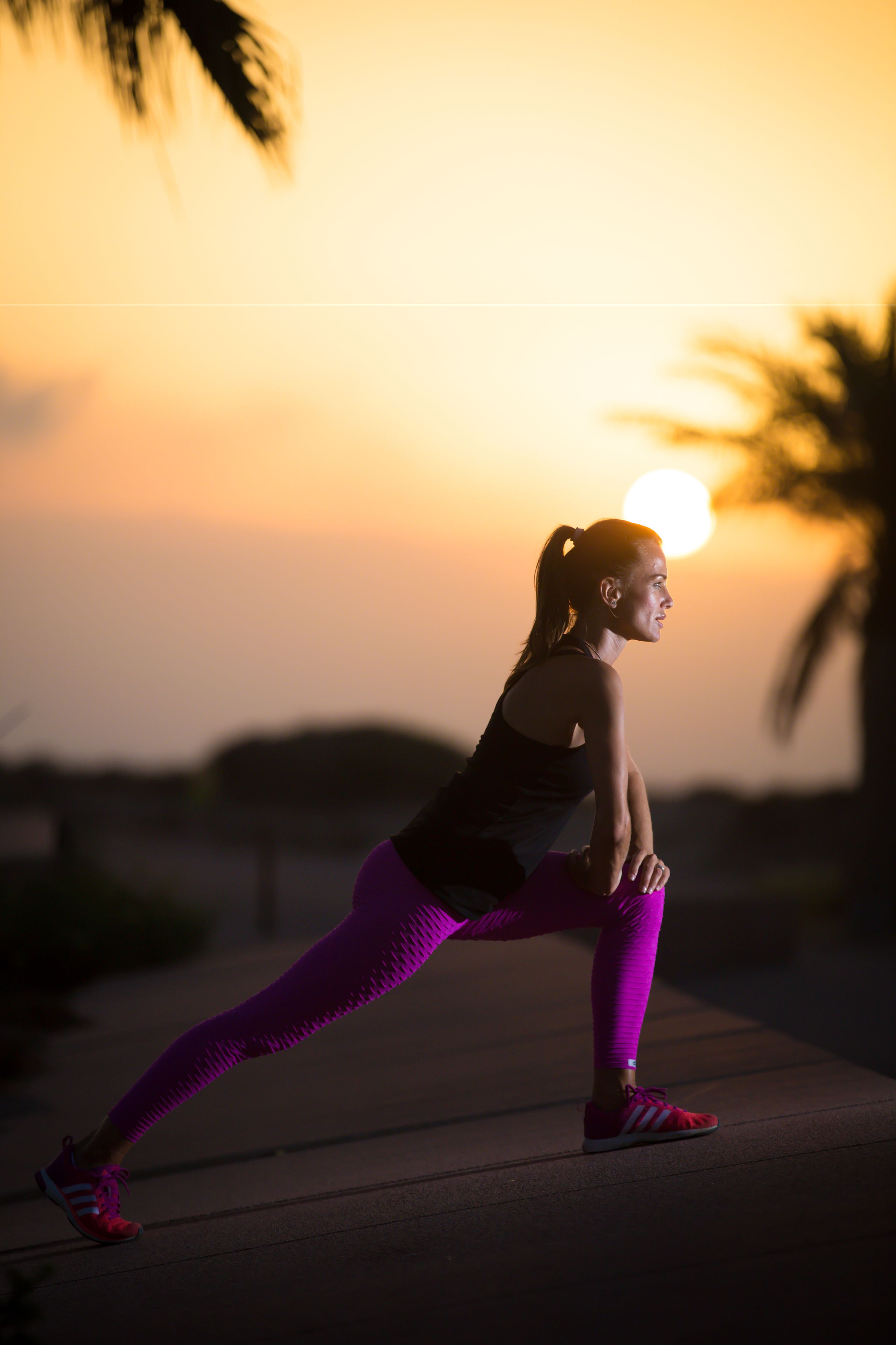 A person in a lunge position on a pathway with a sunset in the background.