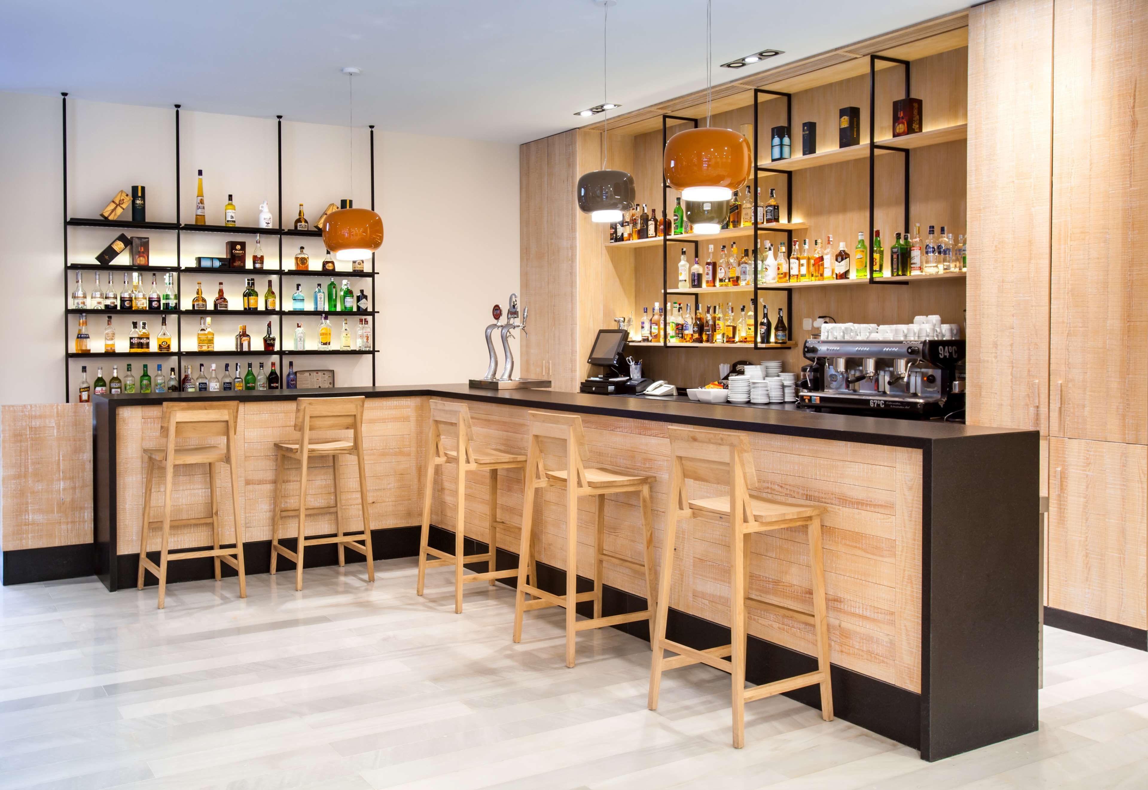 A modern bar with wooden bar stools, shelves of liquor bottles, and a coffee machine.