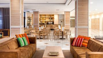 A modern hotel lobby with leather sofas, wooden paneling, a bar area, and a spacious seating arrangement.