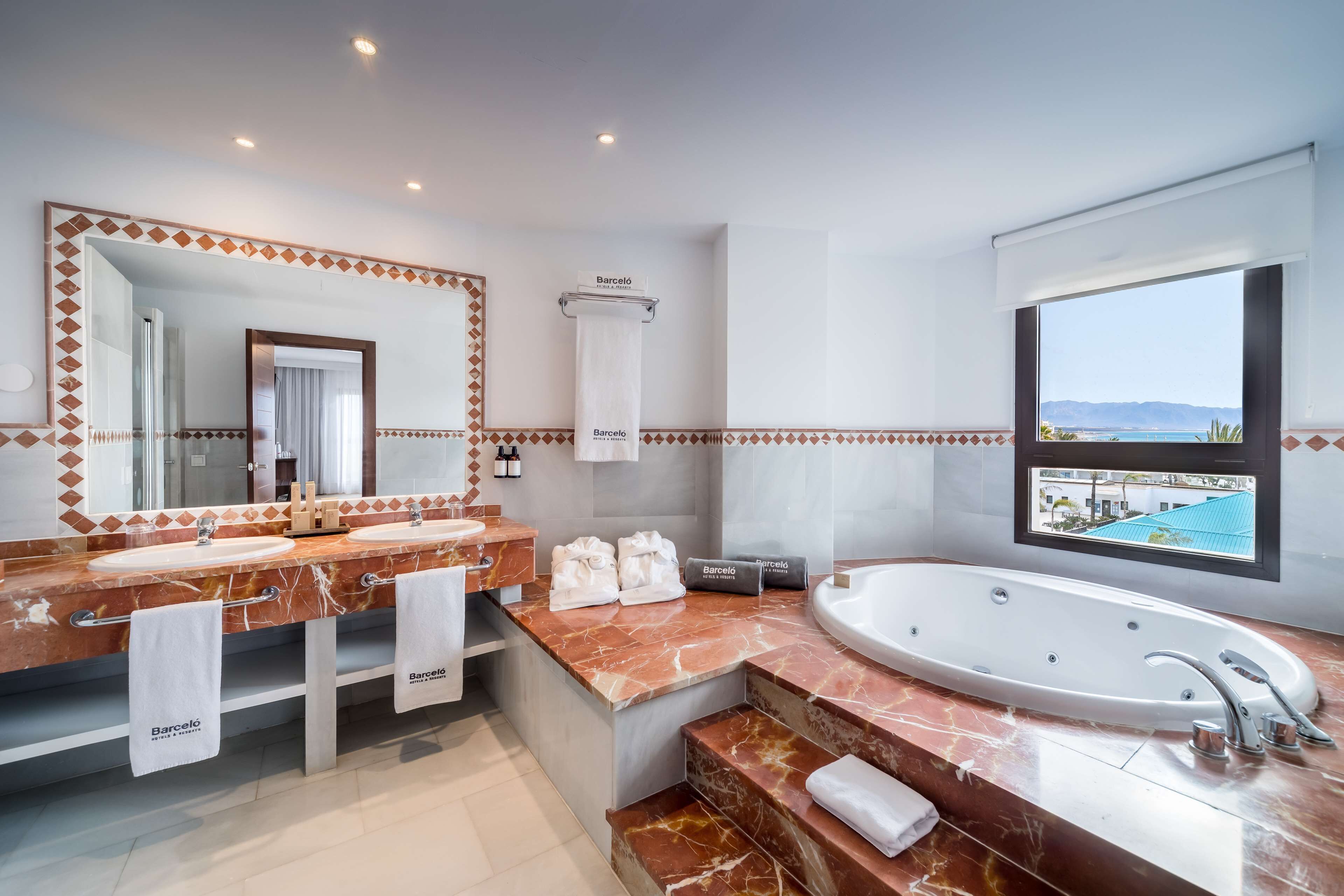 A modern bathroom with dual sinks, a large bathtub, and a view of the sea.
