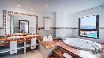 A modern bathroom with dual sinks, a large bathtub, and a view of the sea.