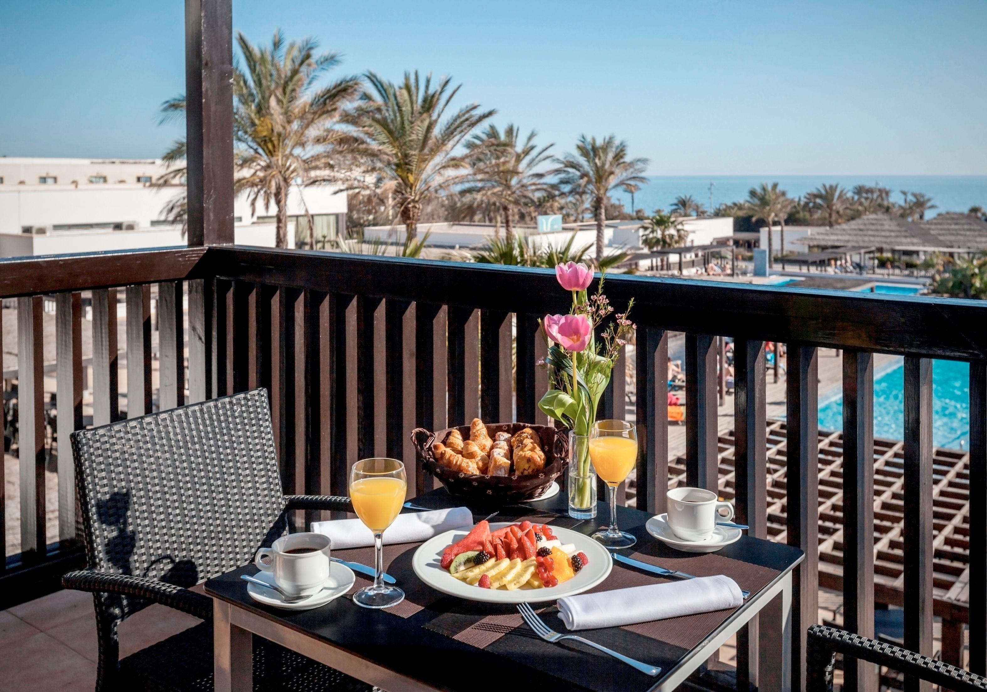 A balcony with a table set for breakfast, including croissants, fruit, and beverages.