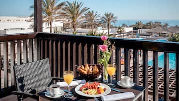 Un balcón con una mesa lista para el desayuno, incluyendo cruasanes, fruta y bebidas.