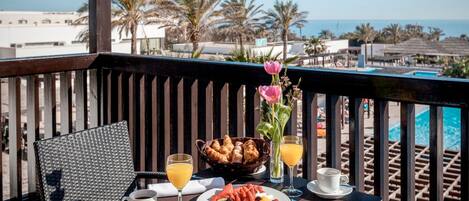 A balcony with a table set for breakfast, including croissants, fruit, and beverages.