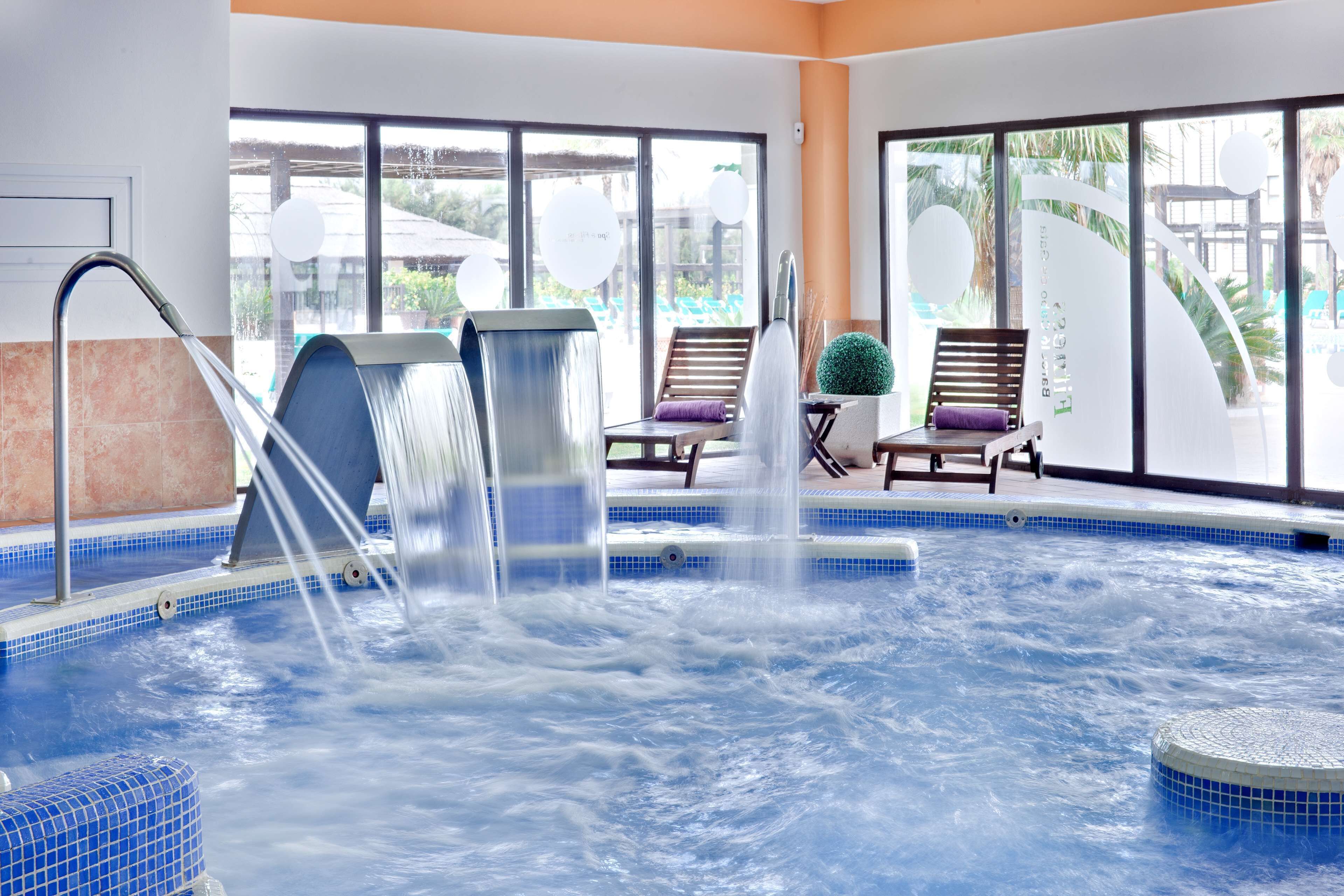 A hot tub with water jets, surrounded by lounge chairs and a view of a pool area.
