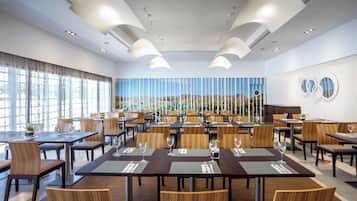 A modern dining area with multiple tables and chairs, large windows, and a view of the desert landscape.