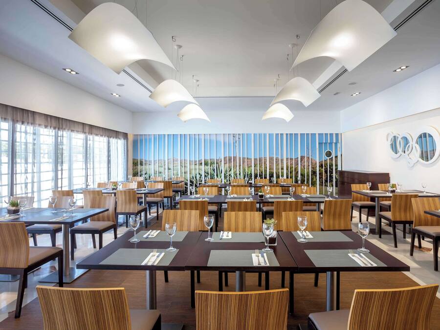 A modern dining area with multiple tables and chairs, large windows, and a view of the desert landscape.