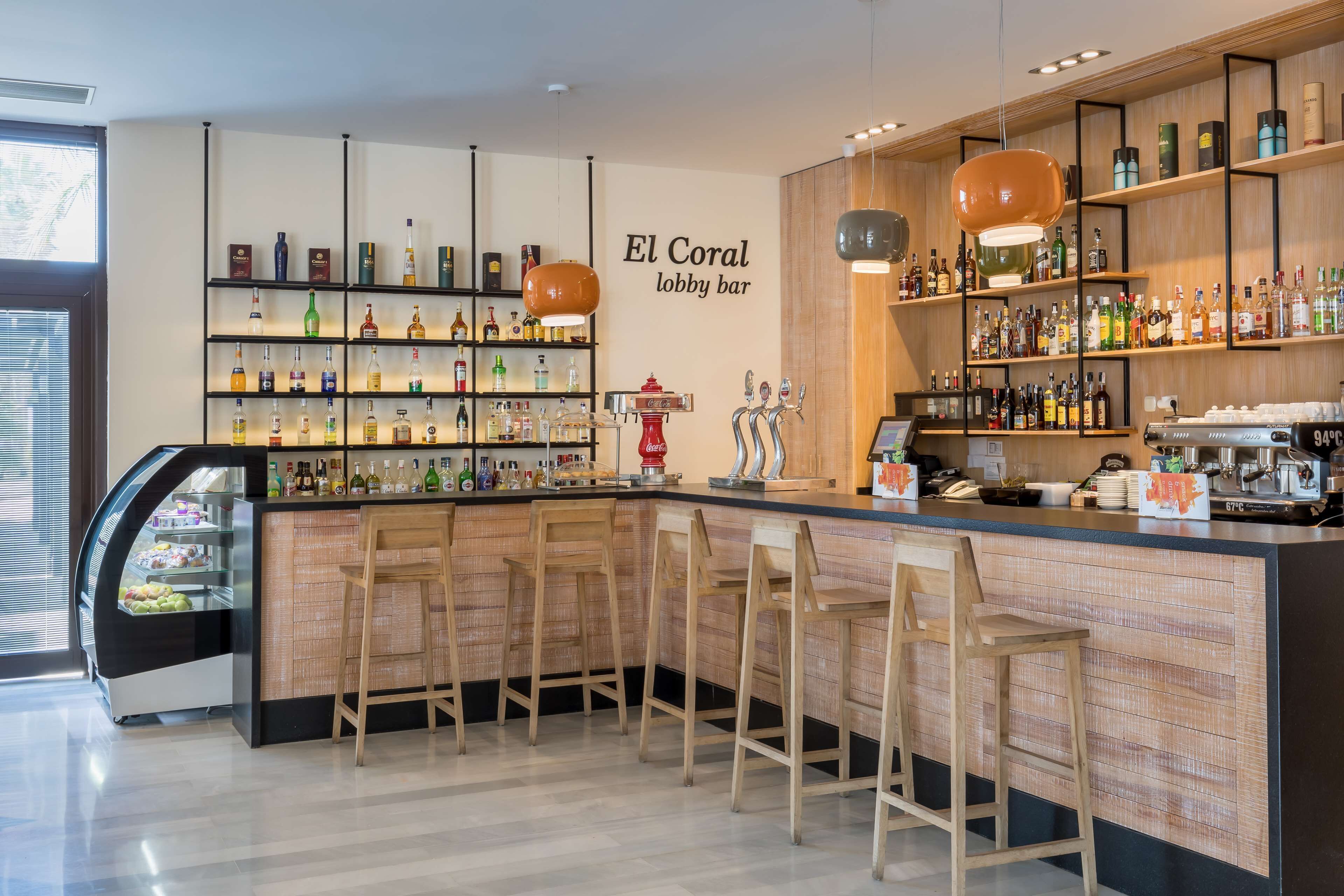 A bar with a wooden bar counter, multiple stools, and shelves stocked with bottles.