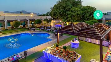 Un patio de hotel con piscina, mobiliario exterior y una zona cubierta.