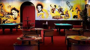 A billiards room with multiple tables and chairs, a red carpet, and a mural with billiards-related artwork.