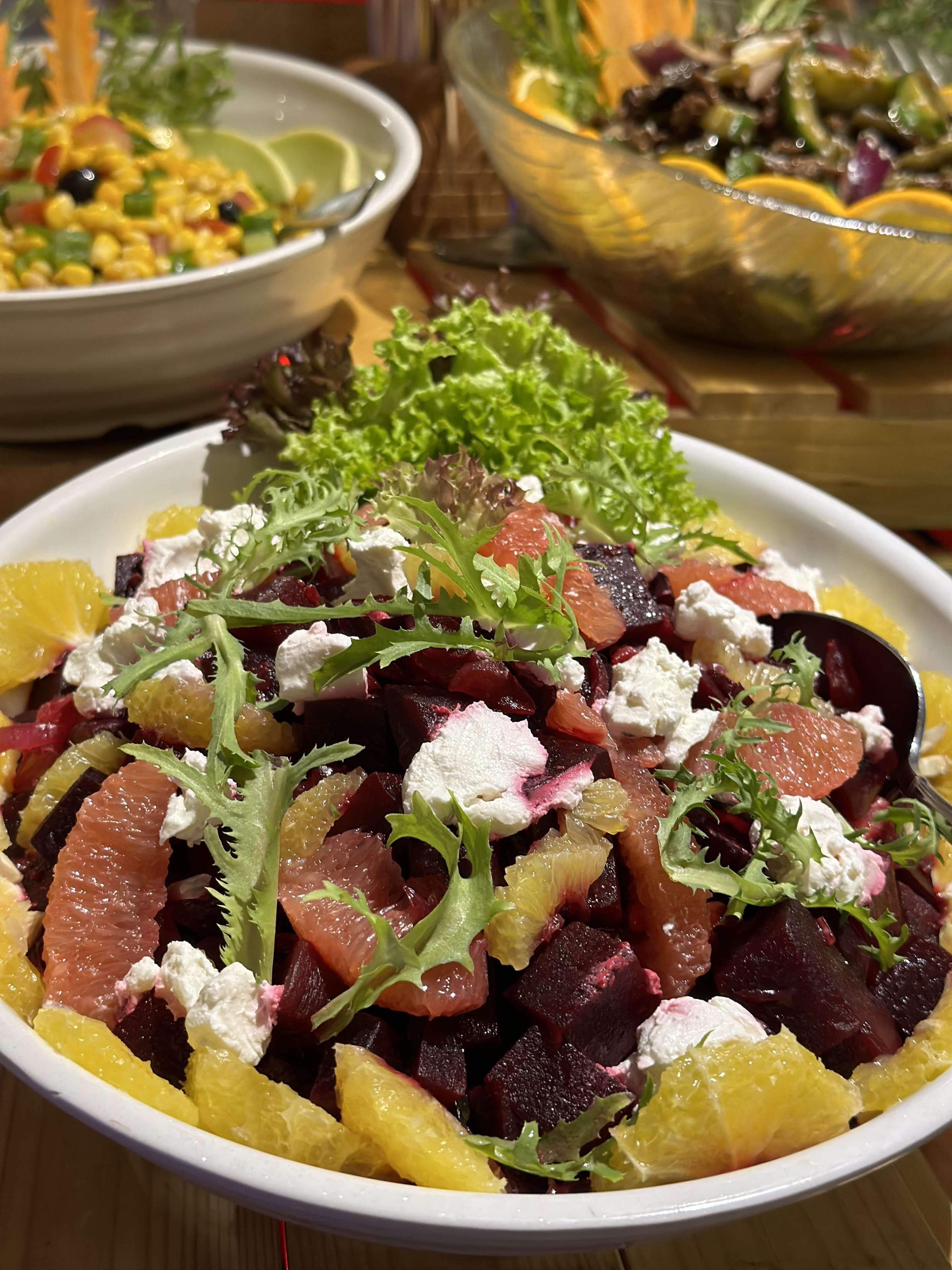 A bowl of salad with various ingredients and a bowl of soup in the background.