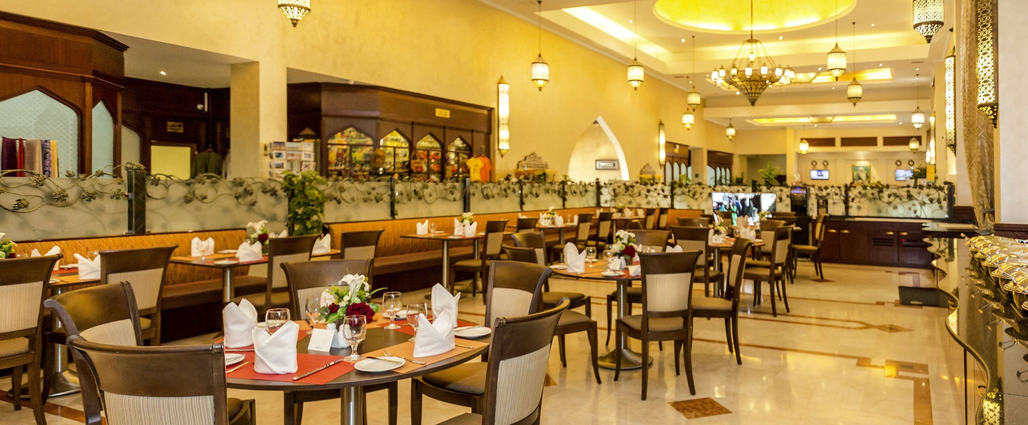 A well-lit restaurant with multiple tables and chairs, a counter area, and decorative wall elements.