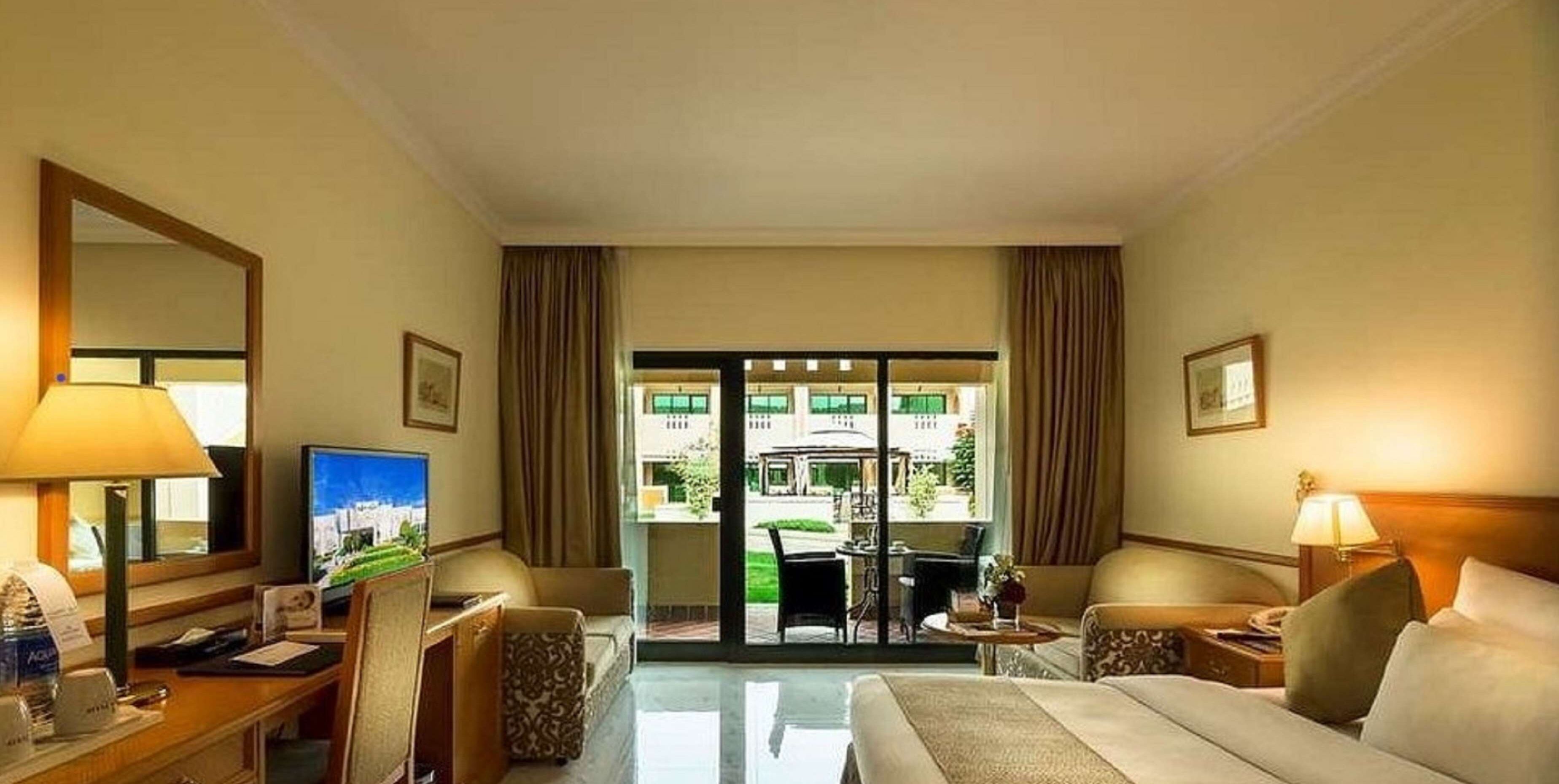 A hotel room with a bed, a desk with a computer, a television, and a view of the outside.