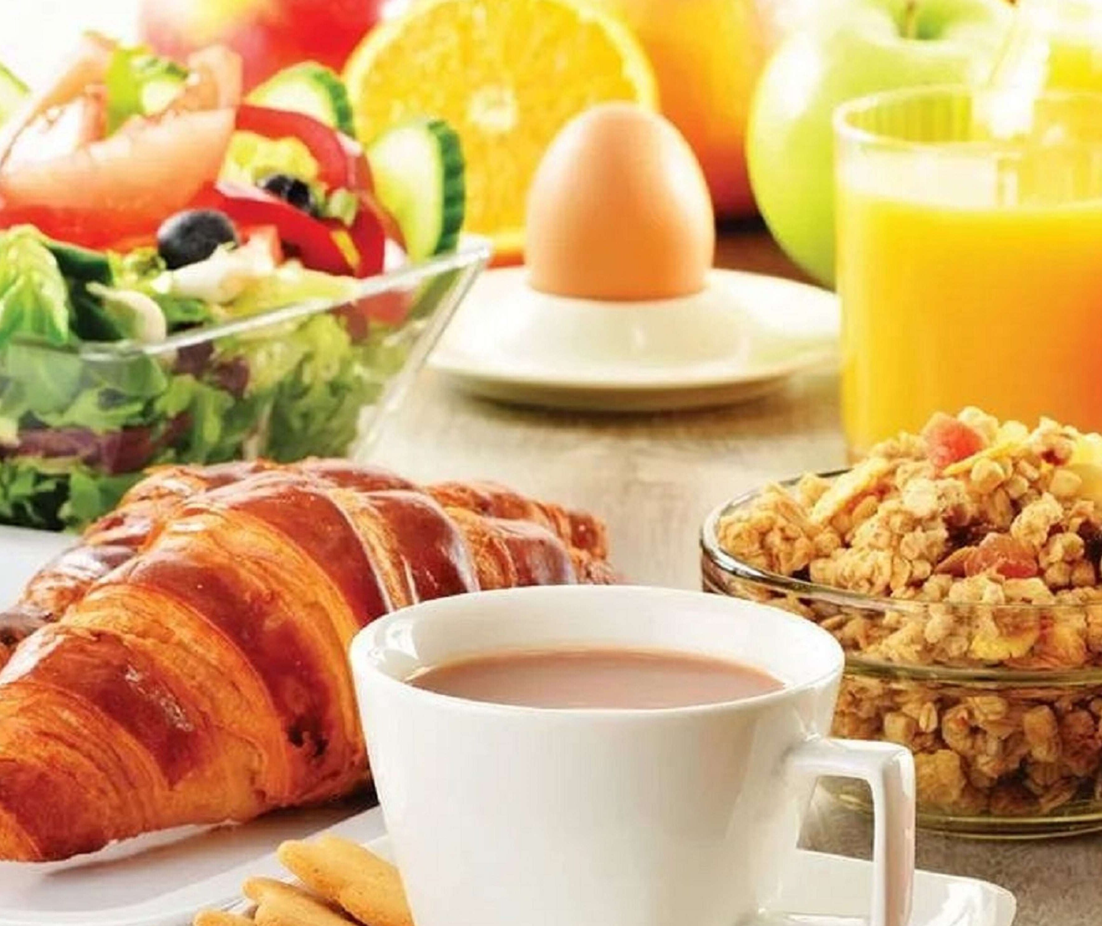 A breakfast setting with a croissant, coffee, cereal, and fresh fruits.