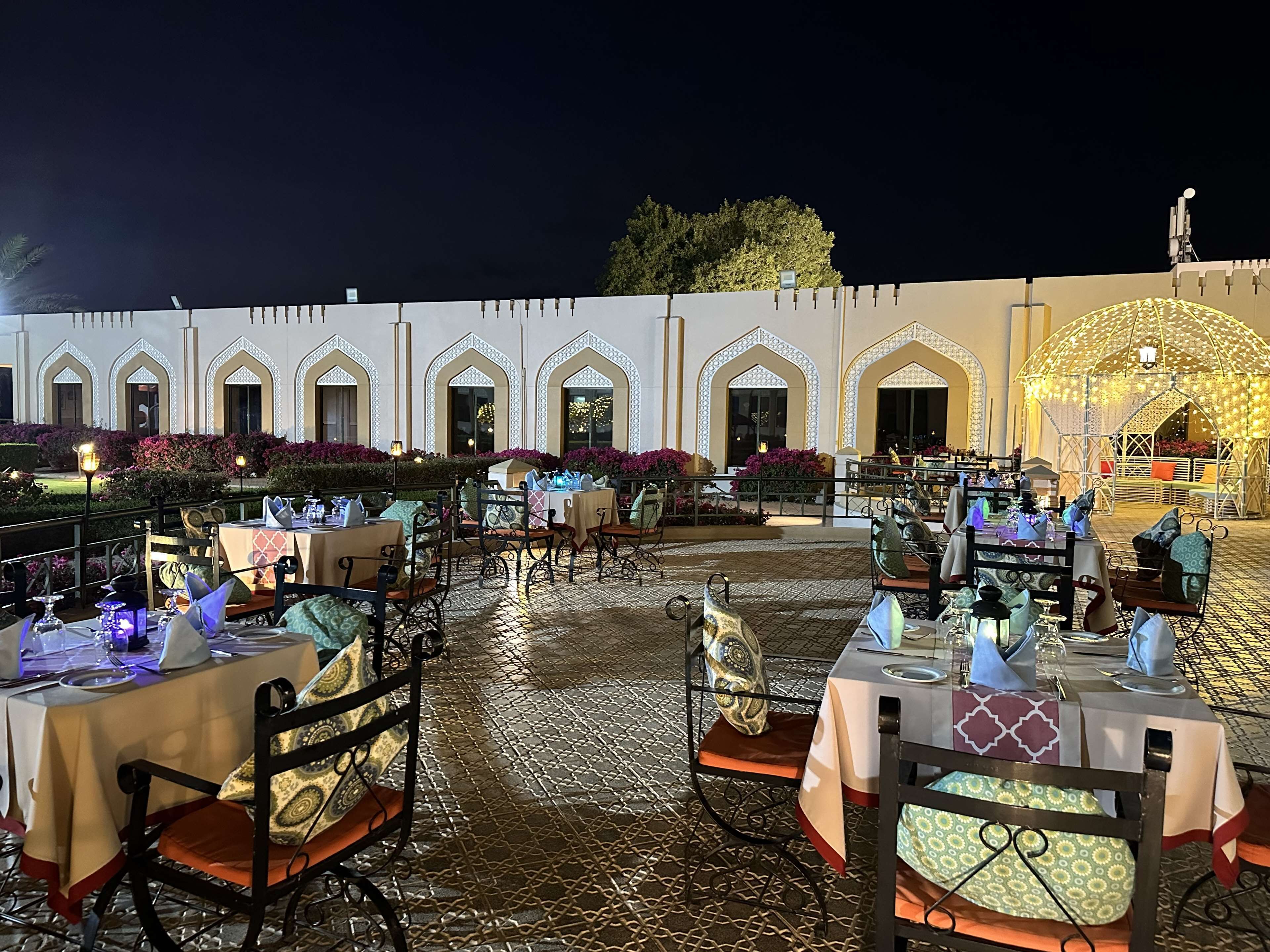 An outdoor dining area with tables and chairs, a patterned floor, and a building with arched windows in the background.
