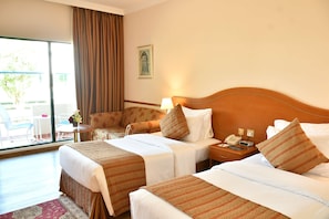 A hotel room with two beds, a small table, a chair, and a large window with curtains.