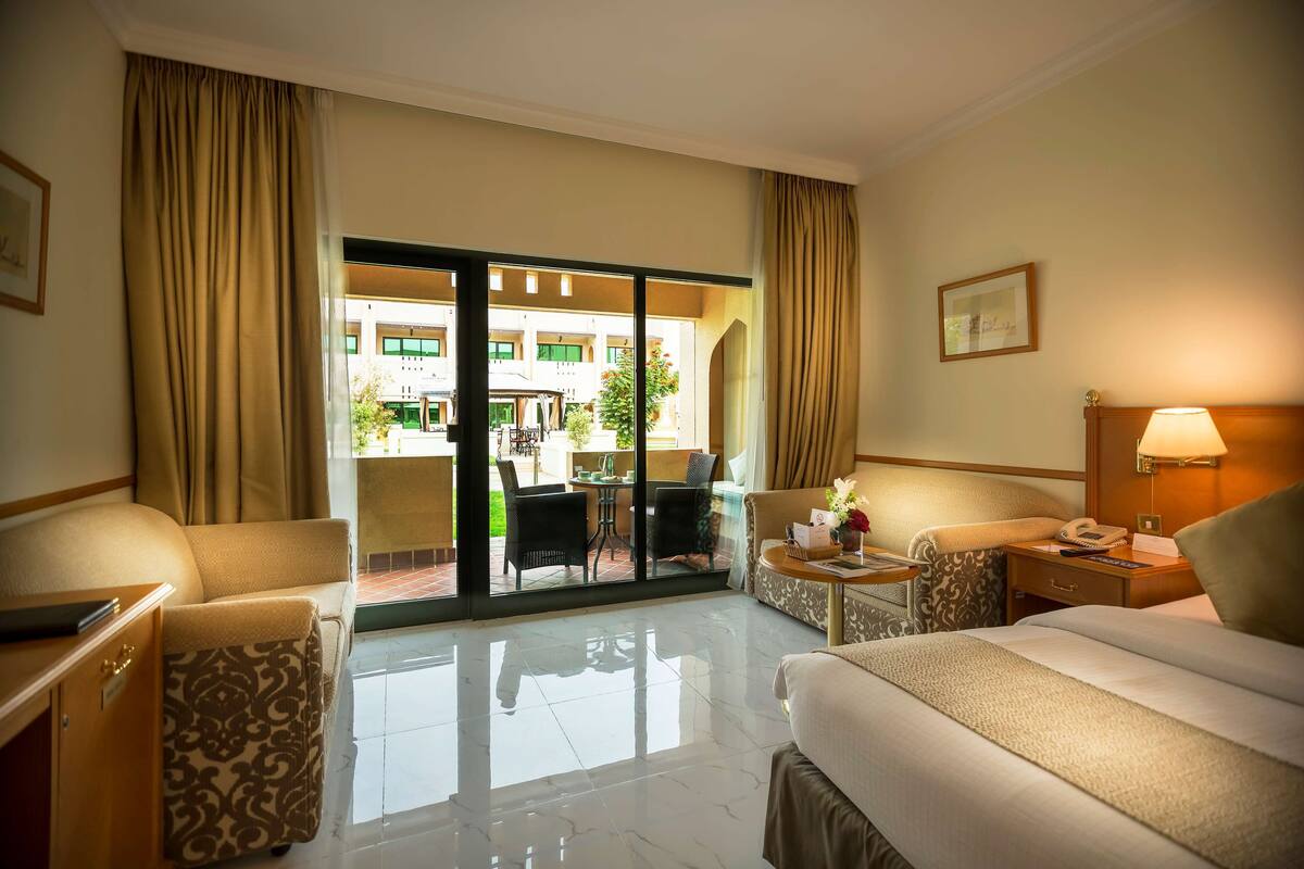 A hotel room with a bed, a desk, a chair, a small table, and a view of the outdoor area.