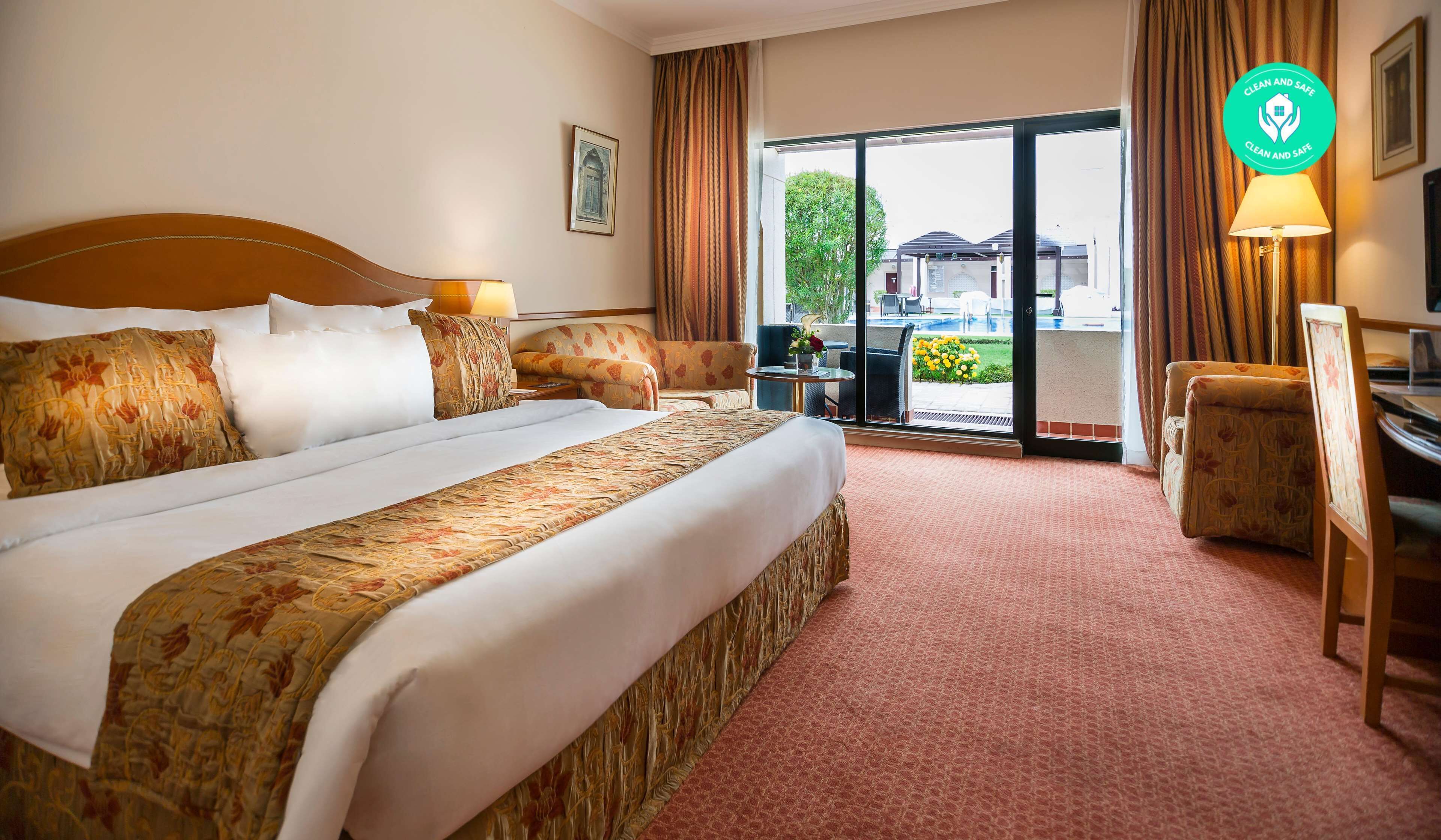 Une chambre d’hôtel avec un grand lit, un bureau, une chaise et une vue sur une piscine et la verdure environnante.