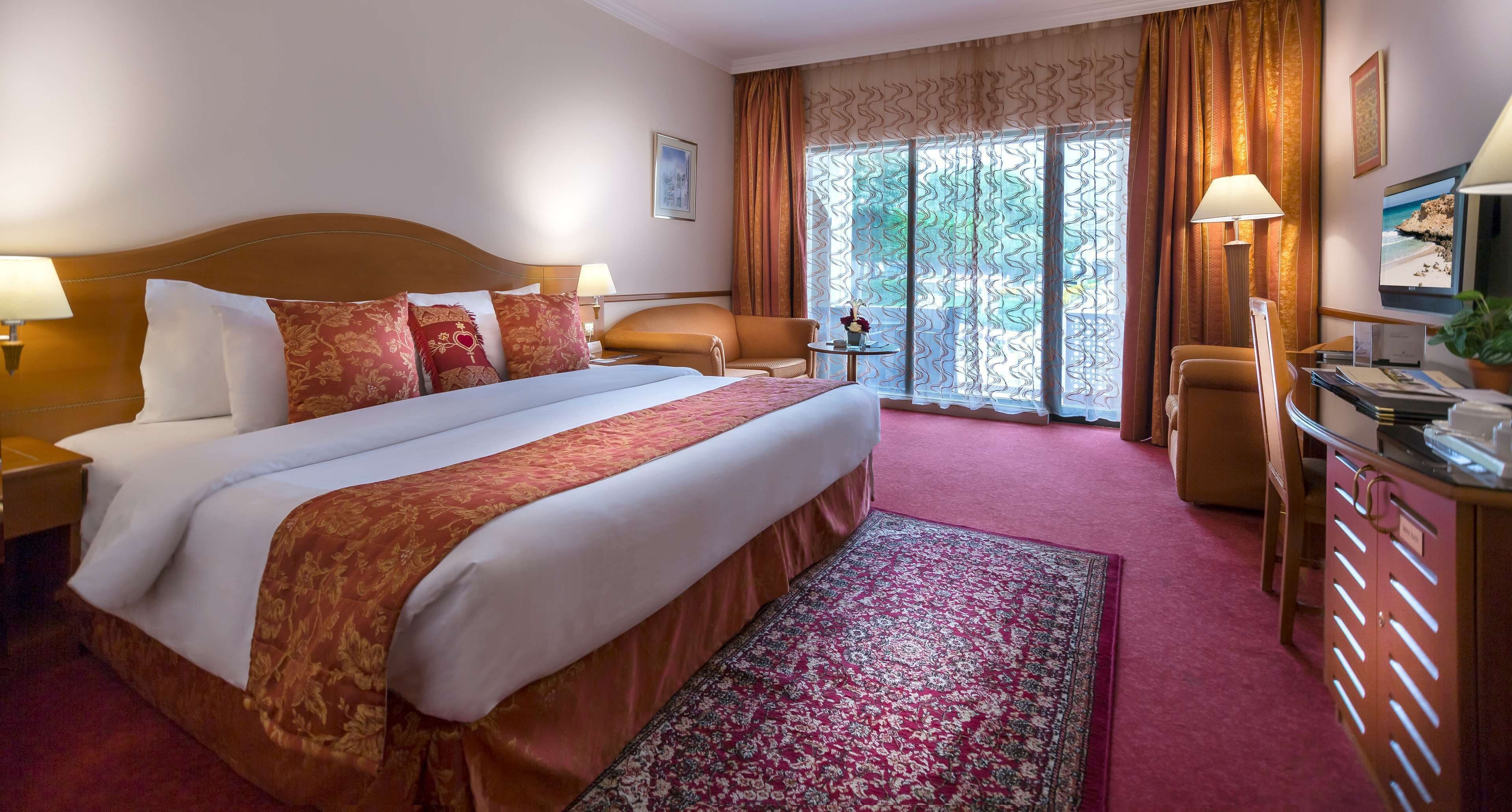 Une chambre d’hôtel avec un grand lit, un bureau, une chaise et une vue sur l’extérieur par une fenêtre.