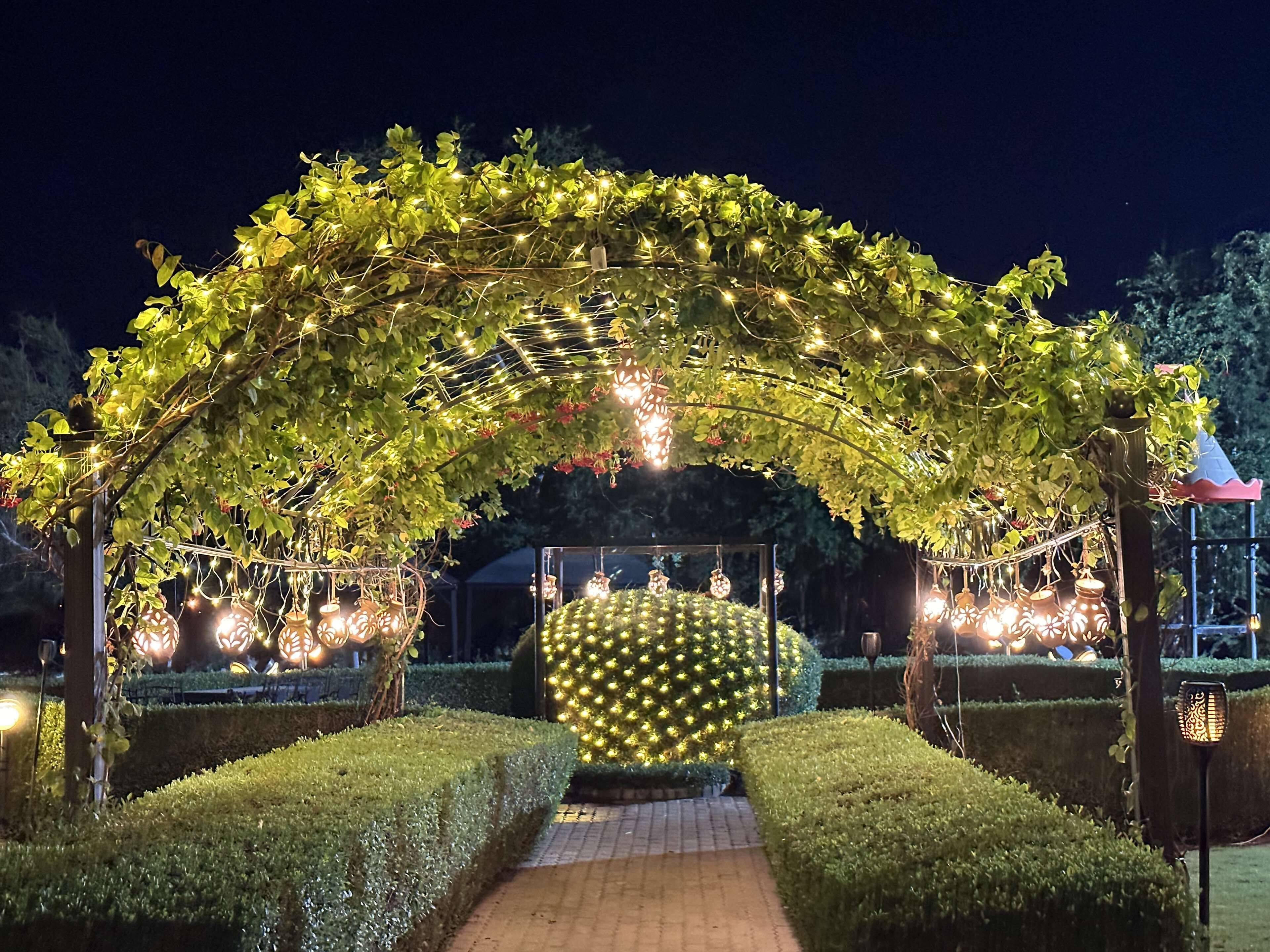 Un sendero de jardín con un arco decorativo adornado con luces y follaje.