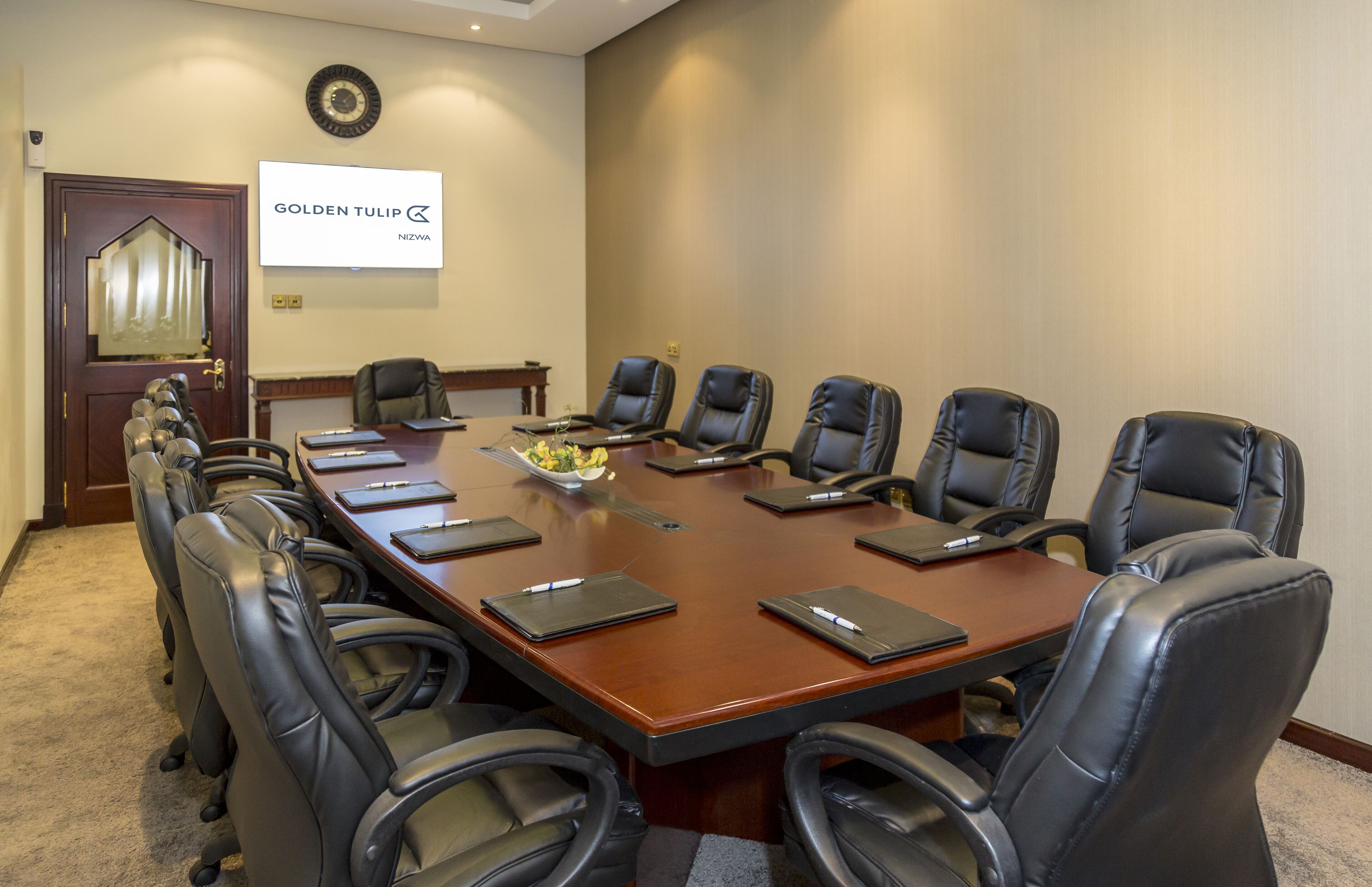 A conference room with a long table, eight black leather chairs, and a whiteboard on the wall.