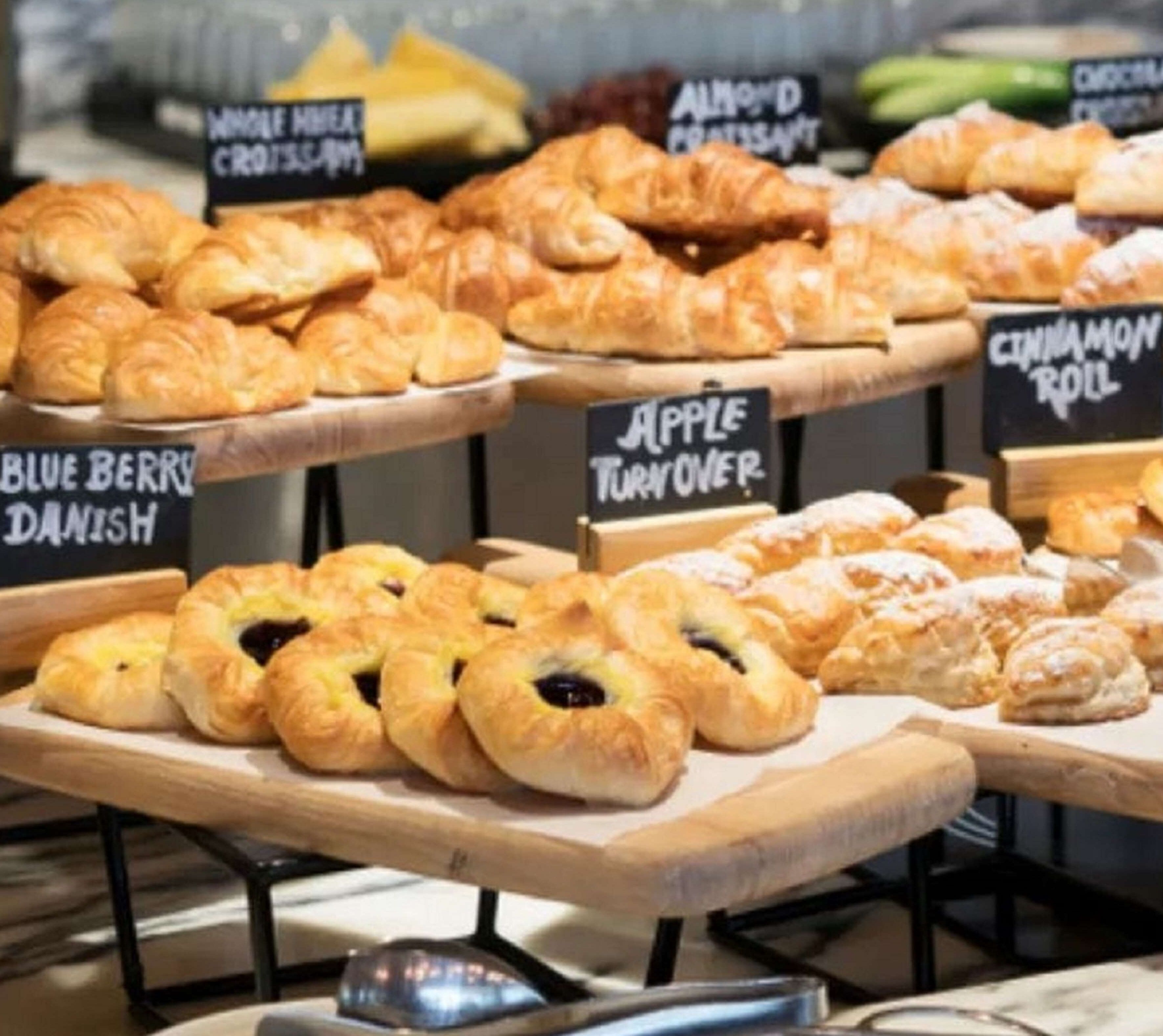 Mostrador de pastelería con diferentes tipos de productos, como hojaldre de manzana, rollos de canela y danesas de arándanos.