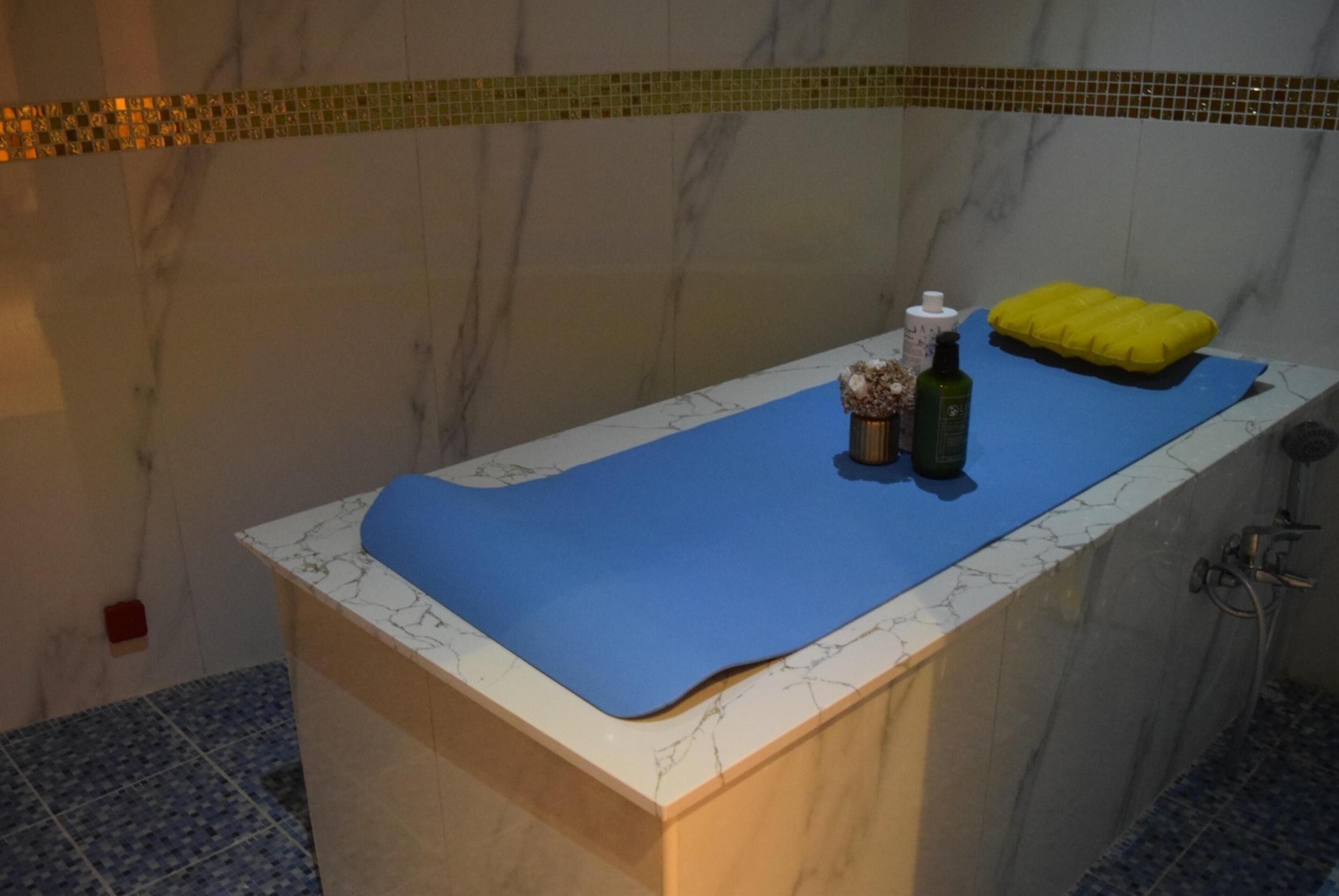 Un bagno con un piano in marmo, un tappetino blu e un tappetino da bagno giallo, e una bottiglia d'olio d'oliva.