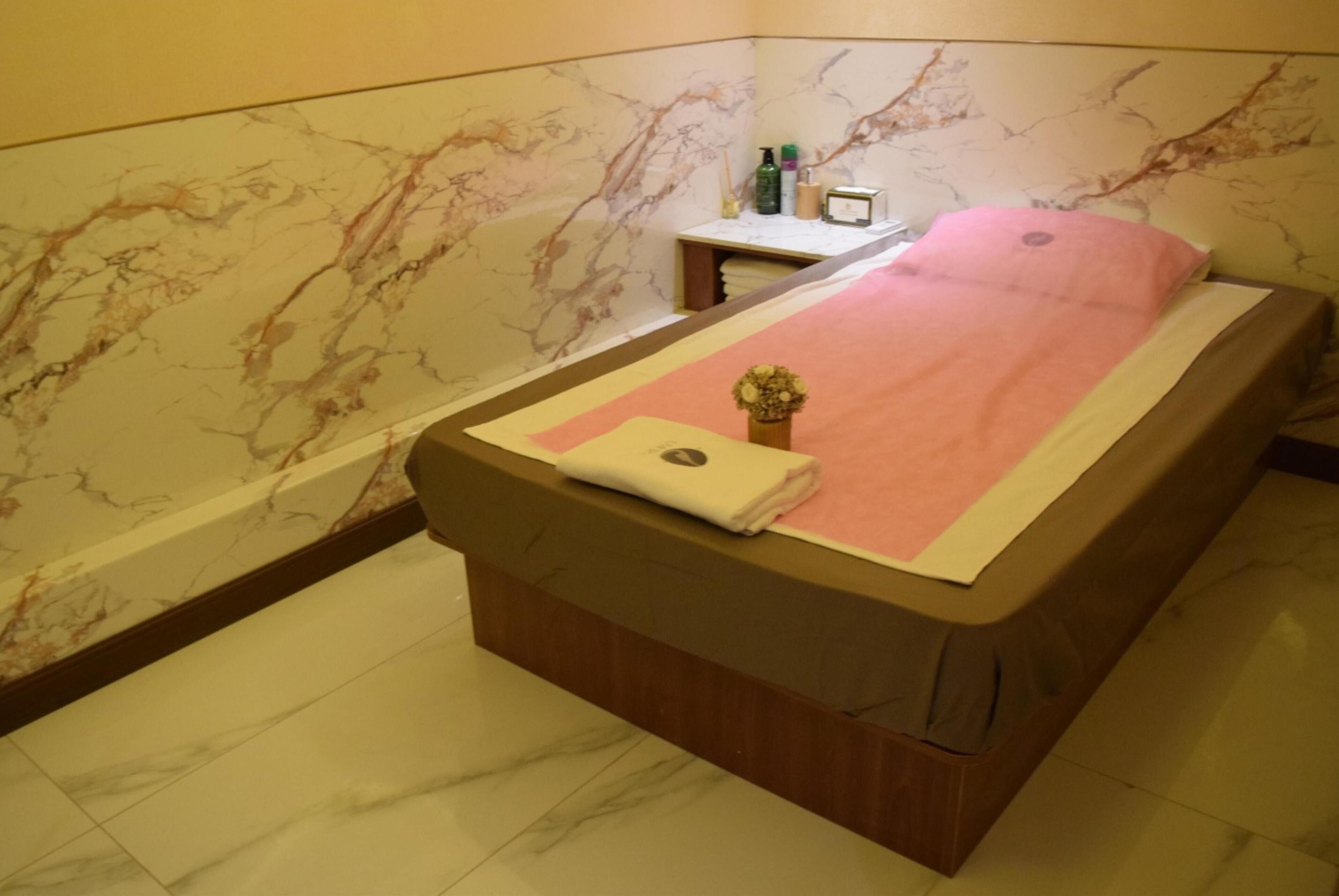 A neatly made bed with a pink blanket and a small vase of flowers.