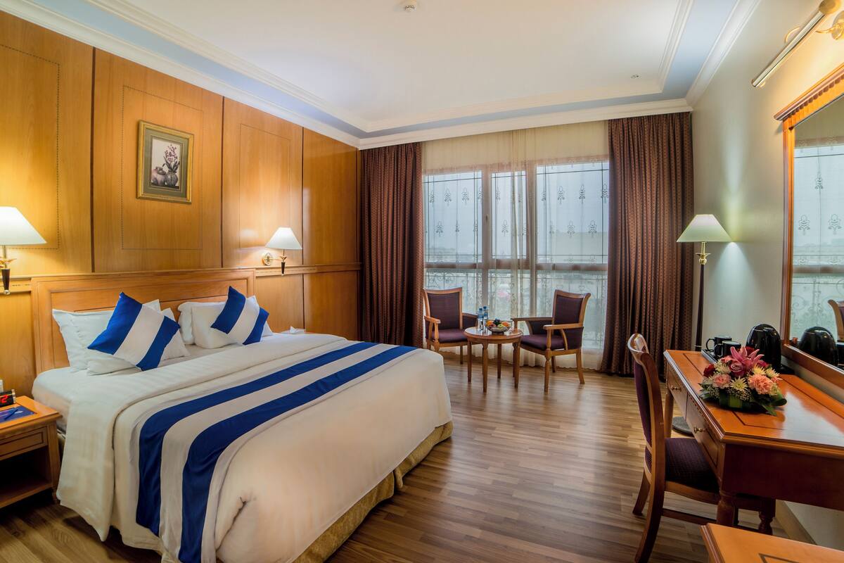 Een hotelkamer met een groot bed, twee stoelen, een bureau en een raam met gordijnen.