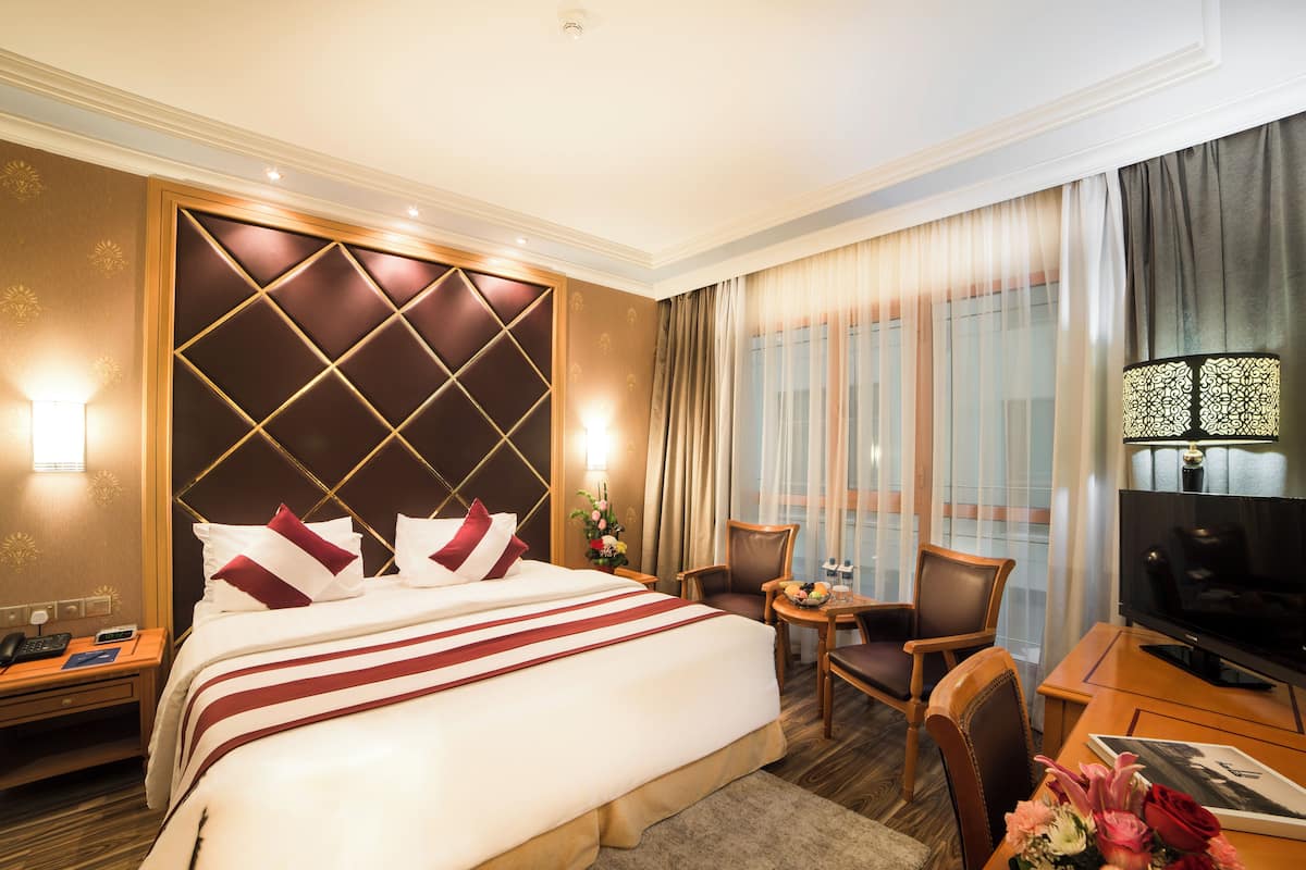 Een hotelkamer met een groot bed, twee stoelen, een bureau, een televisie en een raam met gordijnen.