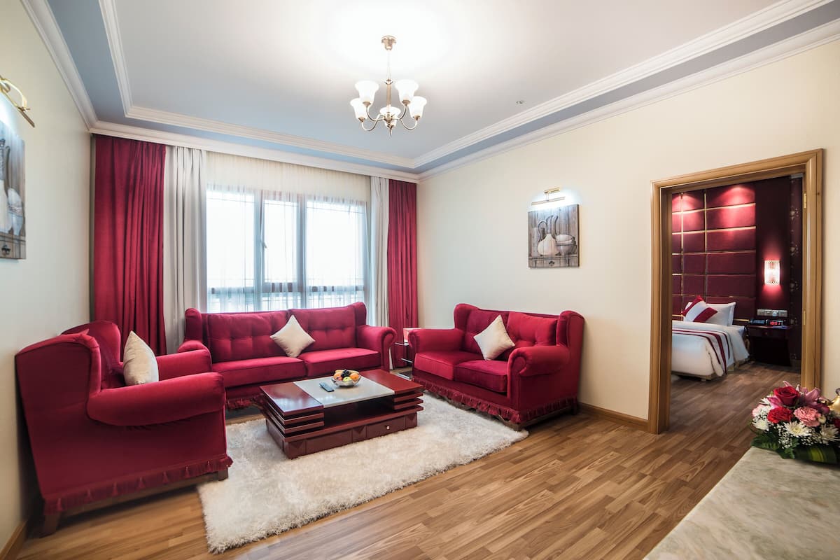 Een ruime woonkamer met een rode bank, een zacht, wit tapijt en een houten salontafel.