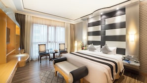 Quarto de hotel com uma cama grande, mesas de cabeceira, escrivaninha e um espaço de estar.