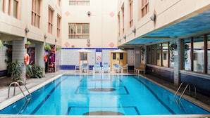 Piscina interna com paredes revestidas, aviso proibindo saltos e áreas de estar.