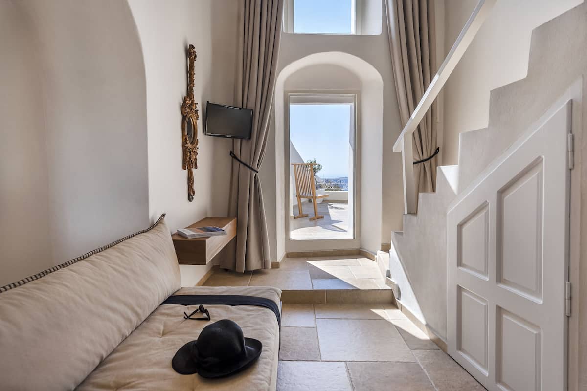 A hotel room with a bed, a TV, a window with curtains, and a view of the beach.
