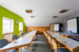 Un salón de conferencias con una larga mesa, sillas, una pizarra y una pantalla para proyector.