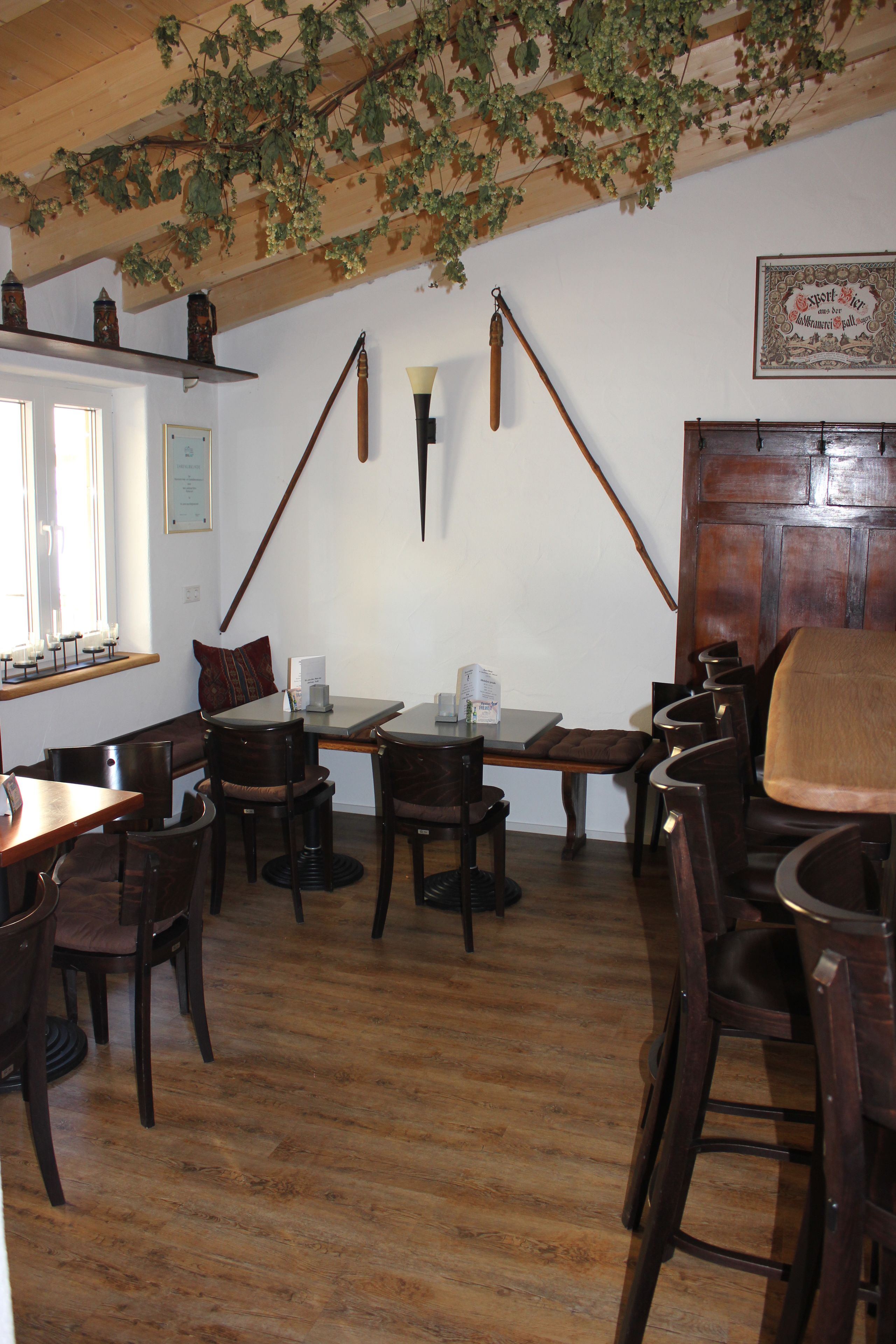 Una posada tradicional con pisos de madera, un techo alto adornado con hiedra colgante y una decoración rústica que incluye una puerta de madera y faroles en la pared.