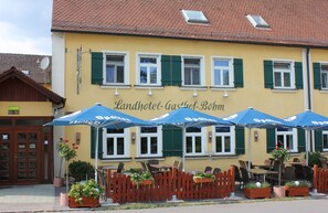 A building with outdoor seating and umbrellas, a wooden fence, and potted plants. - Landhotel Zum Böhm (Roth)