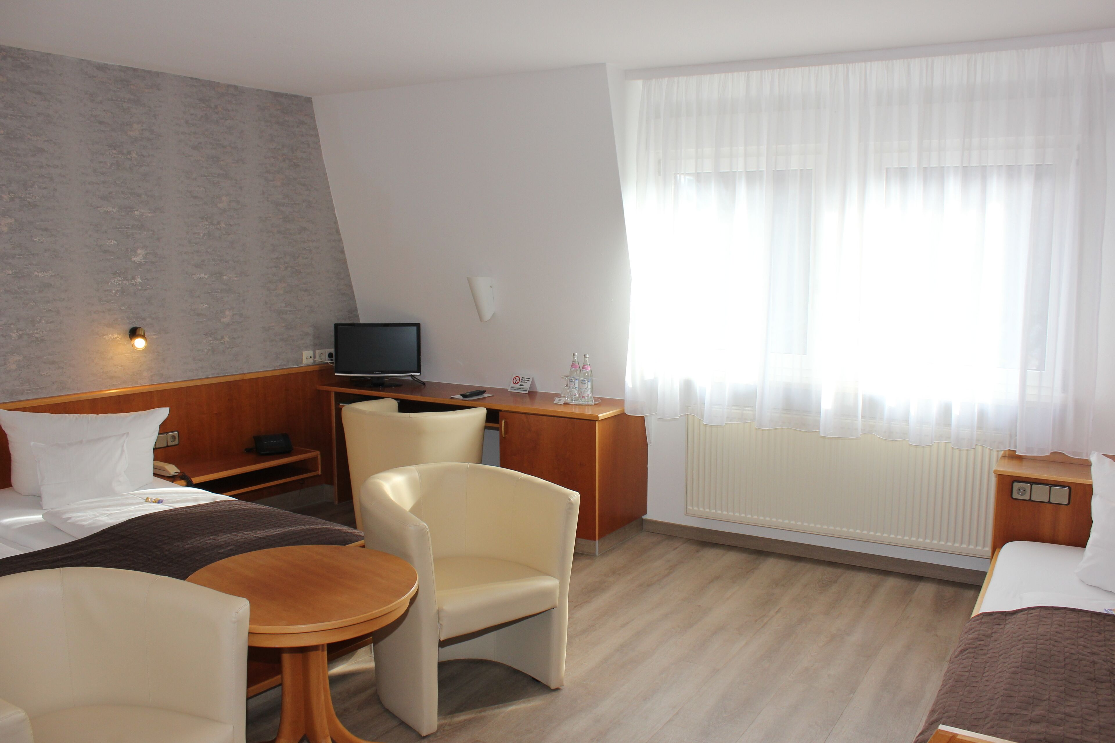 Ein Hotelzimmer mit Bett, Schreibtisch, Stuhl, kleinem Tisch und Fernseher.