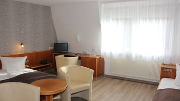 Quarto de hotel com cama, escrivaninha, cadeira, mesinha e televisão.
