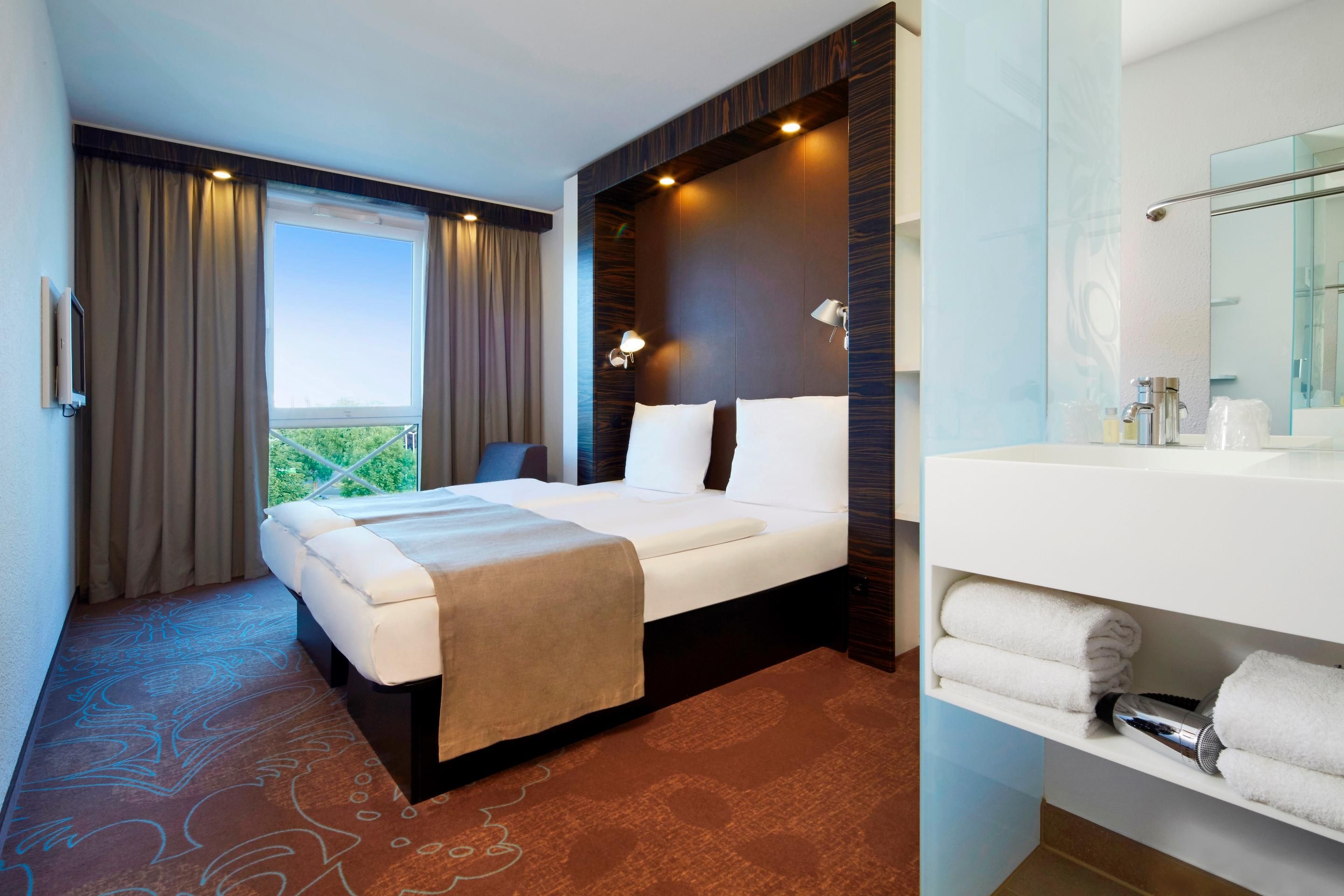 Una habitación de hotel con cama, baño con espejo y vistas por la ventana.
