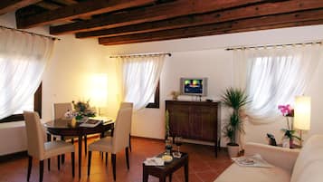 Una sala de estar con un sofá, dos sillas, una mesa de centro, un televisor y una mesa de comedor con un florero.