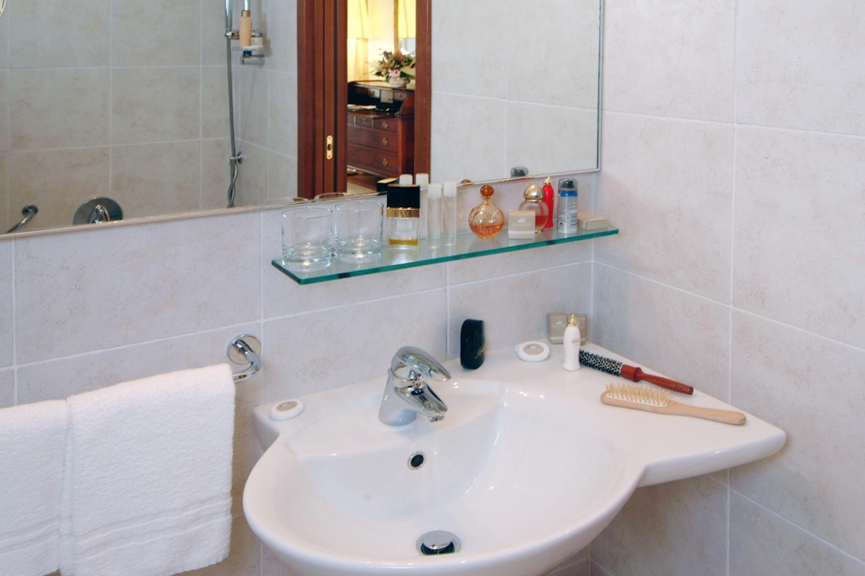 A bathroom with a white sink, a mirror, and a glass shelf above it.