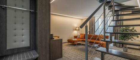 A modern interior with a staircase, a sofa, a lamp, and a plant.