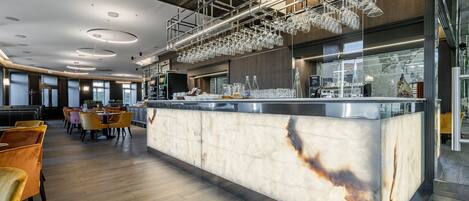 A modern bar area with a marble countertop, overhead glassware holders, and seating in the background.