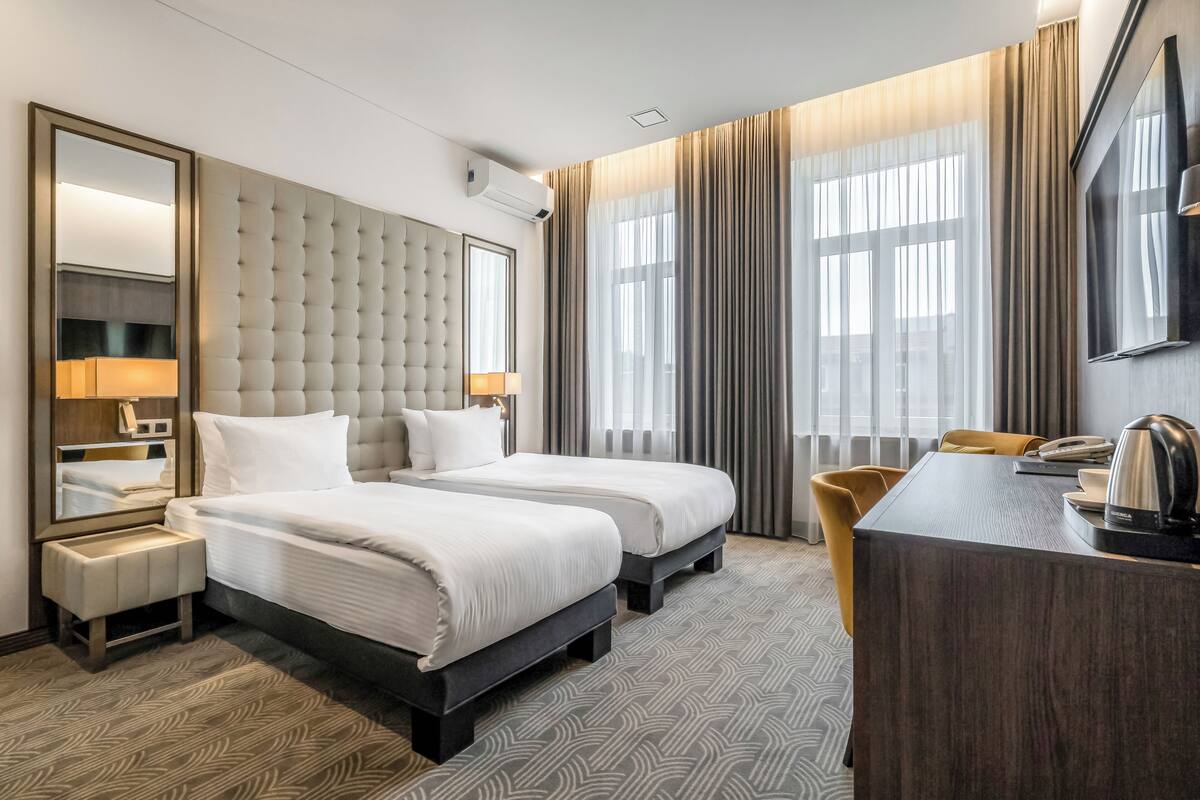 Camera d'albergo con due letti, una scrivania, una sedia, uno specchio grande e una televisione.