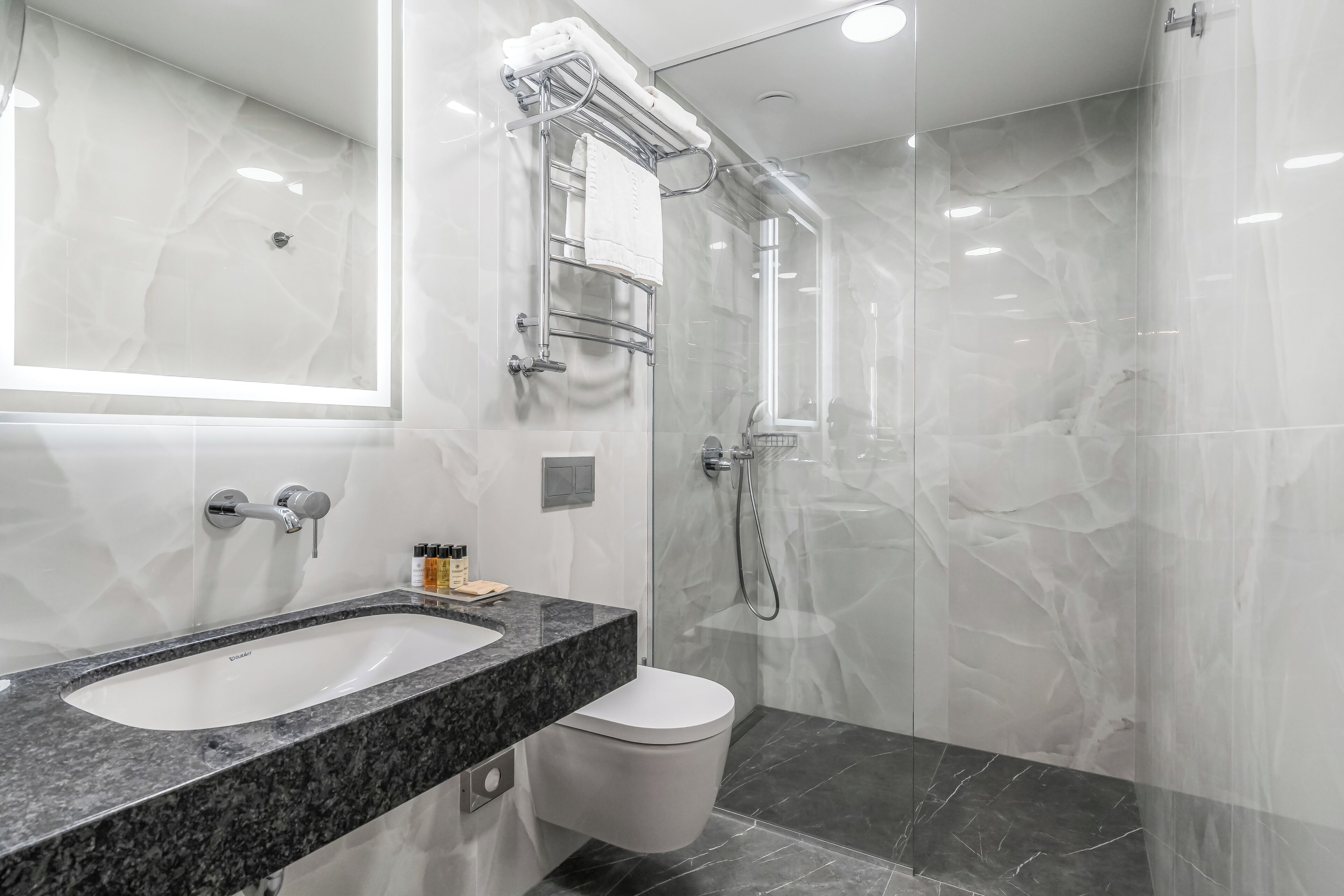 Un baño moderno con lavamanos de mármol, inodoro y ducha con mampara de vidrio.