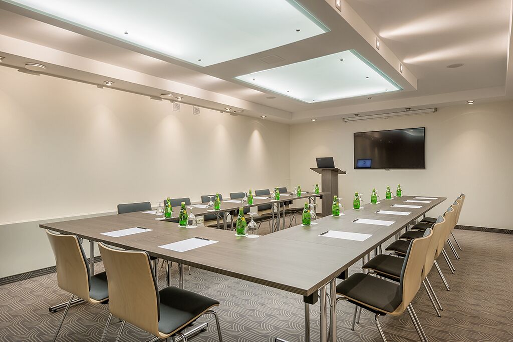Une salle de conférence avec une longue table, des chaises, un téléviseur à écran plat et des luminaires au plafond.