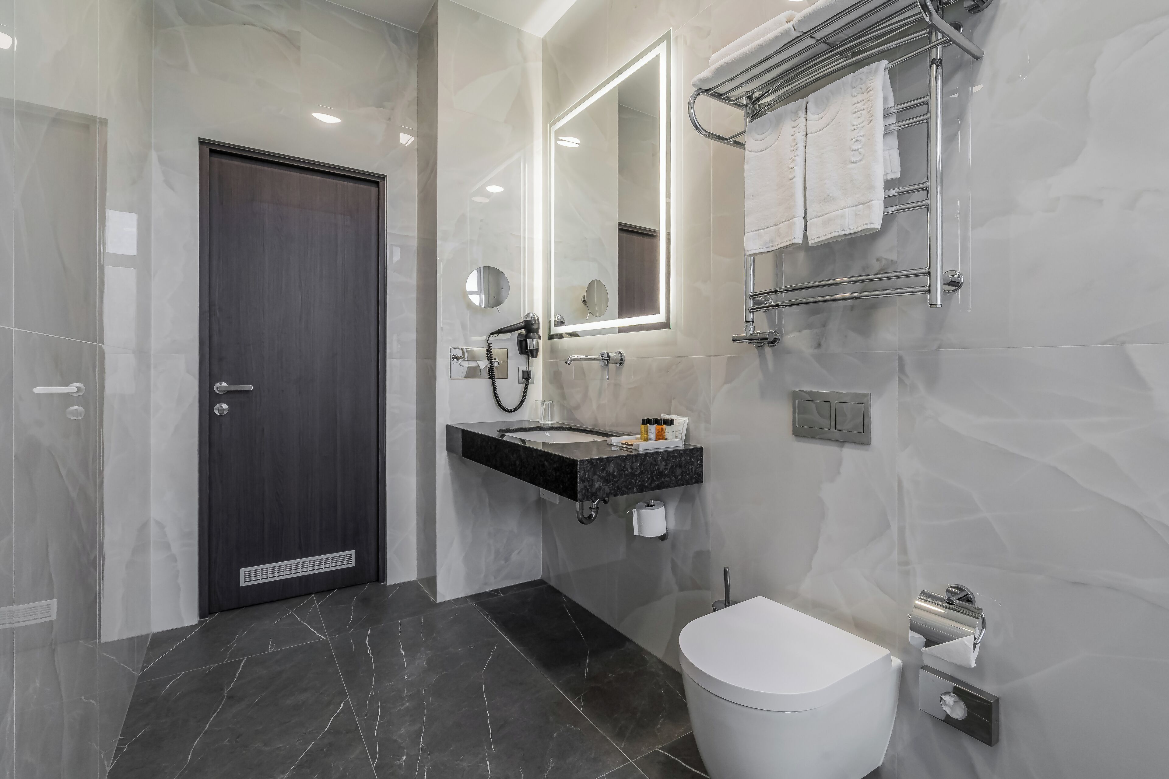 A modern bathroom with a dark door, a vanity with a mirror, a towel rack, and a toilet.