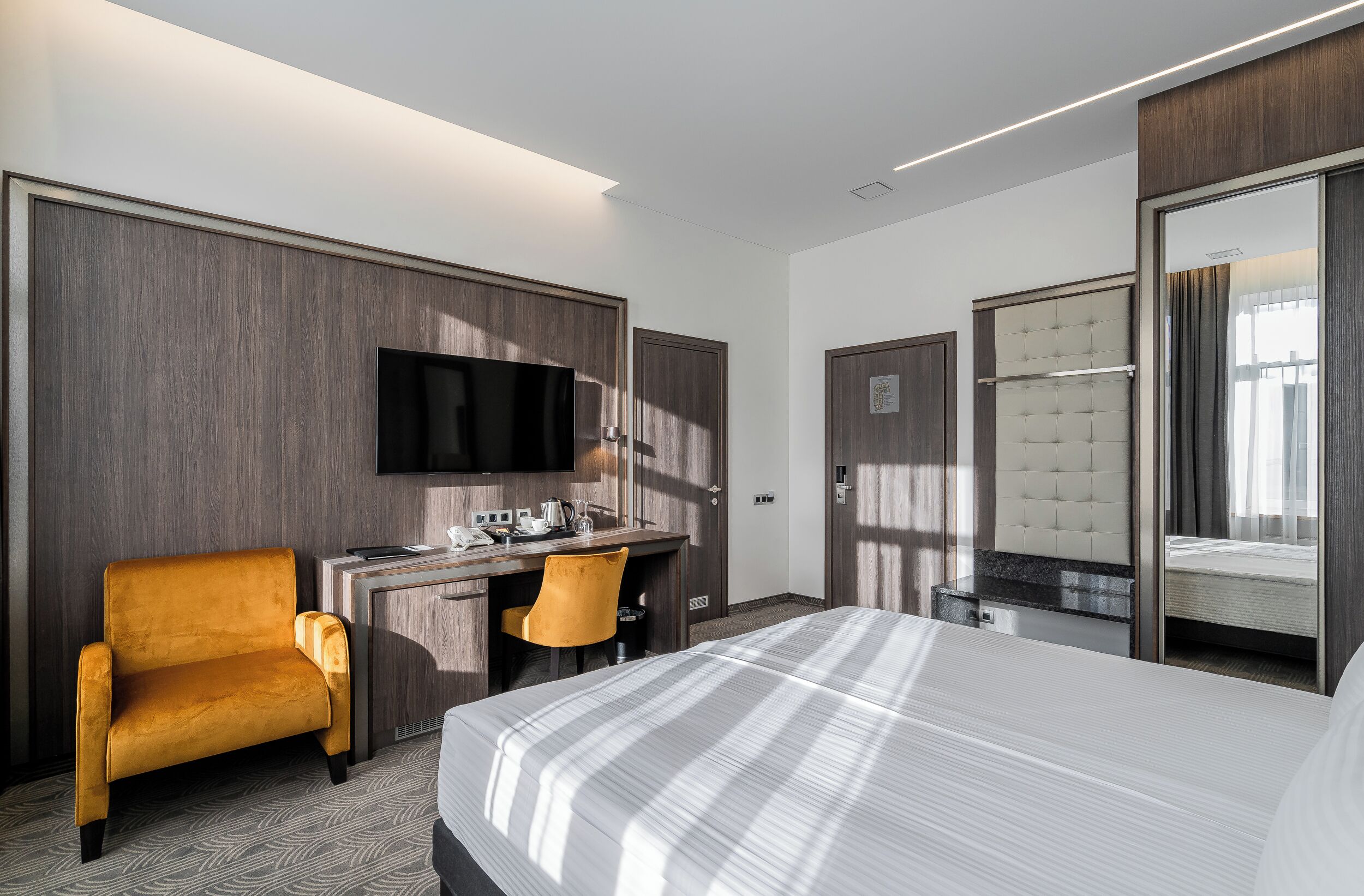 A hotel room with a bed, a desk with a chair, a television, and a wardrobe.