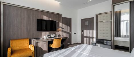 A hotel room with a bed, a desk with a chair, a television, and a wardrobe.